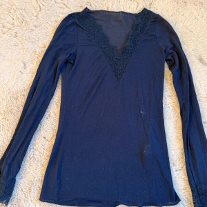 Mörkblå långärmad topp med spets - Mörkblå långärmad topp från Intimissimi med djup v-ringning dekorerad med spets. Toppens ärmslut har också spetsdetaljer som ger en extra touch. Tunn och mjuk, perfekt för lager-på-lager eller som statement-piece.