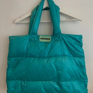 Turkos axelväska från Rockandblue - Stor och fluffig turkos shoppingväska från Rockandblue med vadderade handtag och coolt leopardmönstrat innerfoder. Väskan är tillverkad i syntetmaterial och dun som vaddering och har dragkedja upptill. Perfekt för dig som vill sticka ut med en färgglad accessoar.