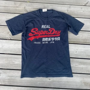 Super Dry T-shirt - Den är i fin fint skick ändats lite rynkor i loggan. Tröjan är i storlek S men passar som XS. Den har en härlig basfärg och sedan en logga i röd färg som får den att sticka ut. Axelbred: 45cm längd från toppen till botten: 58cm. Det är bara att höra av sig om man har några frågor eller om man vill ha flera bilder.