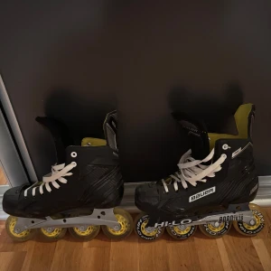 Svarta Bauer inlines med gula hjul - Säljer ett par svarta Bauer inlines med vita snören och gula hjul. Skorna har högt skaft och insida i gul textil, samt robust snörning för bra stöd. Perfekta för dig som vill glida fram på gatan med stil och kontroll. Använda 5-6 gånger och är i bra skick. Finns några synliga skrapmärken men annars väldigt bra skick. 