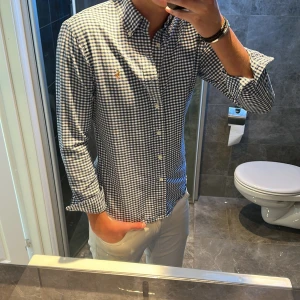 Rutig skjorta från Ralph Lauren - Säljer en klassisk rutig skjorta från Ralph Lauren i blått och vitt. Skjortan har lång ärm, knappar hela vägen och den ikoniska broderade loggan på bröstet. Jag är 188cm och bär storlek S på bilden. Hör av er vid funderingar;)