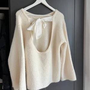Vit stickad tröja med rosett i ryggen - Superfin vit stickad tröja med breda ribbade ränder och öppen rygg som knyts med en stor rosett. Tröjan har lång ärm och loose passform!Ny utan prislapp💕🥰