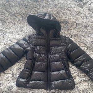 Svart pufferjacka med huva  - Säljer en svart pufferjacka med huva från lager157.Jackan har vattenavvisande yta, dragkedja framtill och två sidofickor med dragkedja. Perfekt för kyliga dagar och riktigt skön passform. Fodrad och lätt att bära. Beställde fel storlek