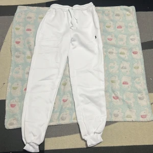 Vita mjukisbyxor från Polo Ralph Lauren S 152-156 cm - Snygga vita mjukisbyxor från Polo Ralph Lauren med klassisk broderad logga i svart på benet. Byxorna har resår och snörning i midjan samt muddar vid bensluten för en skön och avslappnad passform. Perfekta för chill eller streetwear.