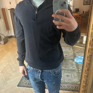 Mörkblå half zip tröja Oscar Jacobson - Snygg mörkblå långärmad tröja från Oscar Jacobson med half zip-dragkedja vid halsen. Tröjan är i klassisk modell med ribbade muddar och är tillverkad i ett mjukt material. Perfekt för en stilren och avslappnad look.