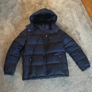 Ralph Lauren puffer - Säljer en mörkblå pufferjacka från Polo Ralph Lauren. Jackan är i rätt fint skick men har några defekter som syns på bilderna. Den är i barnstorlek XL men den passar XS-S vuxenstorlekar. Jackan kostar runt 3200 kronor nypris. Hör av er om ni undrar något. Priset går att diskutera vid snabb affär. 