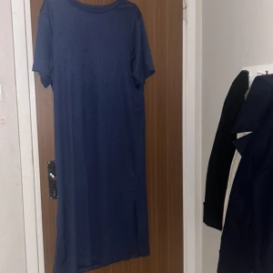 Marinblå långklänning från 157 - Enkel och stilren marinblå långklänning från 157 med korta ärmar och rund halsringning. Klänningen har en rak passform och är tillverkad i ett mjukt, strukturerat material. Perfekt för dig som gillar minimalistisk och avslappnad stil.