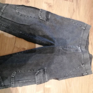 Svarta cargopants från H&M - Säljer ett par svarta cargopants från H&M med coola fickor på sidorna och bak. Byxorna har en avslappnad passform och är gjorda i jeansmaterial, (leggings). Perfekt för dig som gillar streetstyle och vill ha något som sticker ut.