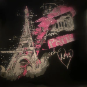 Svart Paris t-shirt med tryck - Svart t-shirt med coolt Paris-tryck, Eiffeltornet och texten 'From Paris with Love' i vitt och rosa. Snygga detaljer med glitter och hjärta. Perfekt för dig som gillar streetstyle och vill sticka ut med en unik look.