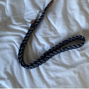 Randigt flätat bälte i blått och vitt - Säljer ett snyggt flätat bälte med randigt mönster i marinblått och vitt. Bältet har detaljer i brunt skinn vid spännet och änden, samt ett metallspänne. Perfekt för att ge outfiten lite extra edge.