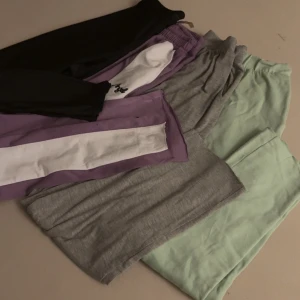 Färgglada mjukisbyxor i olika färger - Fyra par mjukisbyxor i svart, mintgrön, ljusgrå och lila med vit sidopanel. Alla har elastisk midja och är gjorda i mjukt bomullsmaterial, perfekta för chill eller träning. Snygga färger och skön passform för en avslappnad stil.