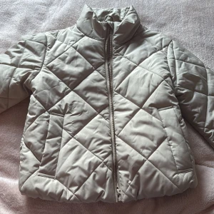 Beige quiltad pufferjacka Samsa Young - Quiltad beige pufferjacka från Samsa Young i storlek 158/164. Jackan har hög krage, dragkedja framtill och två sidofickor. Den har ett stilrent rutmönster och är tillverkad i syntetmaterial som håller dig varm under kyliga dagar.