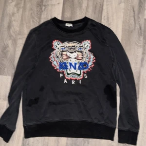 Svart Kenzo sweatshirt med tiger - Svart sweatshirt från Kenzo med ikonisk broderad tiger och färgglada detaljer på bröstet. Tröjan har rund hals, långa ärmar och ribbade muddar. Materialet är mjuk bomull och passformen är normal. Perfekt för dig som vill sticka ut med en cool streetstyle. Passar mig som är 181 storleken passar båda S-M