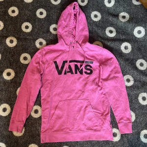 Rosa hoodie från Vans - Säljer en rosa hoodie från Vans med stor svart logga på bröstet. Tröjan har huva med snörning och en klassisk magficka. Långärmad och i mjuk bomull, perfekt för chill dagar. Passar dig som gillar streetwear och färg!