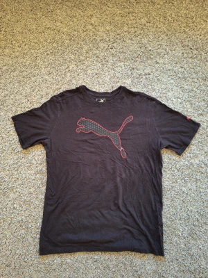Svart Puma t-shirt  - Snygg svart t-shirt från Puma i storlek M. Den har Puma logga på bröstet samt på vänstra ärmen. Tishan har använts många gånger det den har en liten defekt på loggan på bröstet (bild 4). Den har också creasningar då den har legat I lagret länge, men det går bort enkelt med lite strykning. Skick: 7/10