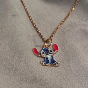 Stitch Halsband Lilo & Stitch Disney smycke guld imitation  - Halsband med gullig liten berlock av Stitch! Trädd på kedja i guldimitation, justerbar 40-45 cm. Berlocken är ca 1,7 x 1,1 cm. 