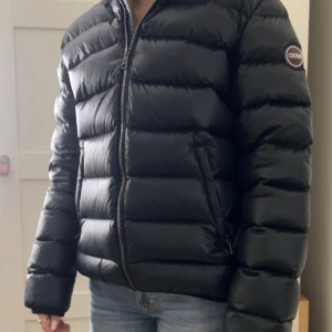 Svart Colmar pufferjacka med huva - Säljer en svart pufferjacka från Colmar Originals med huva och två sidofickor med dragkedja. Jackan har en snygg quiltad look och Colmar-logga på ärmen.  Den är använd fåtal gånger och är i nästan ny kvalité. Sitter som en xs-s. 