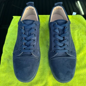 Mörkblå sneakers från Louboutin - Snygga mörkblå sneakers från Louboutin med klassisk röd sula och signatur på undersidan. Skorna har rund tå, snörning och är tillverkade i mocka med detaljer i skinn på insidan. Perfekt för dig som gillar exklusiv streetstyle och vill sticka ut med lyxiga detaljer. Priset kan sänkas vid snabbaffär!