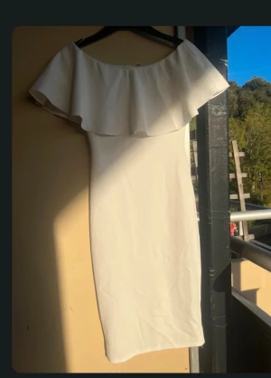 Vit offshoulder klänning med volang - Säljer en stilren vit klänning med offshoulder och bred volang över axlarna. Klänningen är figurnära och har en enkel, elegant design som ger en snygg siluett. Perfekt för dig som gillar minimalistisk stil och vill sticka ut med en trendig look.