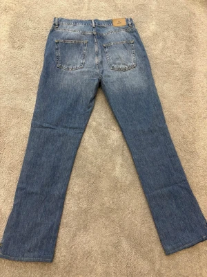 Blå jeans med slits från Nelly - Snygga blå jeans från Nelly med klassisk femficksdesign och raka ben. Jeansen har ljus tvätt och coola slitsar längst ner på benen. Passar dig som gillar en avslappnad stil med lite edge. Perfekt till sneakers eller boots.