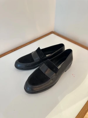 Svarta loafers i skinn och mocka - Snygga svarta loafers från Other Stories med klassisk design. Ovandelen är i mjukt skinn med detaljer i mocka och har en rund tå samt platt sula. Perfekta för dig som gillar stilrena och tidlösa skor med en modern touch. Jag har storlek 39/40 och de är något för små för mig.