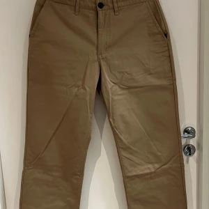 Nike Sb beiga chinos med rak passform - Snygga beiga chinos med klassisk design och raka ben. Byxorna har sidfickor, bälteshällor och stängs med knapp och dragkedja. Perfekta för en clean och stilren look.