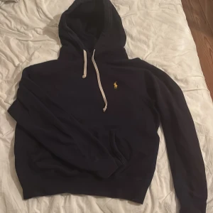 Mörkblå hoodie från Polo Ralph Lauren - Säljer denna snygga mörkblåa hoodie från Polo Raulph Lauren då den är för liten. Den har en känguru ficka och justerbara vita snören. Jag fick denna i julklapp förra året och inte använt så mycket eftersom den var för liten redan då, så den är inte alls mycket använd. PRIS KAN DISKUTERAS 🙌😁
