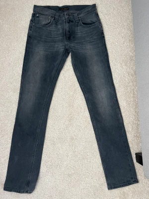 Mörkgrå jeans från Nudie Jeans, 32/34 - Snygga mörkgrå jeans från Nudie Jeans i klassisk femficksmodell. Jeansen är i mycket bra skick och i storleken 32/34. Pris går att diskutera vid snabb affär!