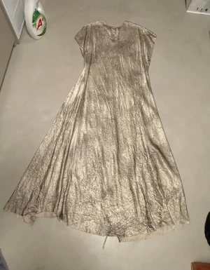 Beige långklänning från Massimo Dutti - Säljer en beige långklänning från Massimo Dutti i storlek L. Kjolen har en glansig och skrynklig yta med ett tunt knytband i midjan för extra stilpoäng. Materialet är lätt och känns lyxigt, perfekt för dig som gillar en elegant och chill vibe.