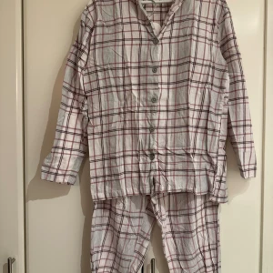 Rutiga pyjamas från Åhléns, stl S - Mysig tvådelad pyjamas från Åhléns i storlek S. Setet är vitt med rosa- och rödrurigt mönster, har skjortkrage, knappar framtill och elastisk midja på byxorna. 