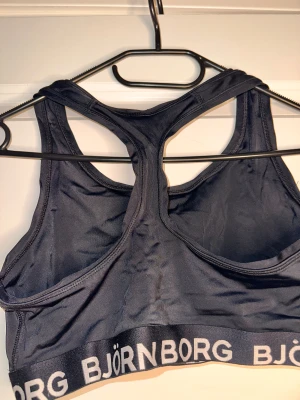 Svart sporttopp från Björn Borg - Sportig svart linnetopp från Björn Borg med brottarrygg och bred resår med logga runt om. Tillverkad i funktionsmaterialet Hydro-Pro som andas och passar perfekt för träning. Snygg och enkel design med stilren look.