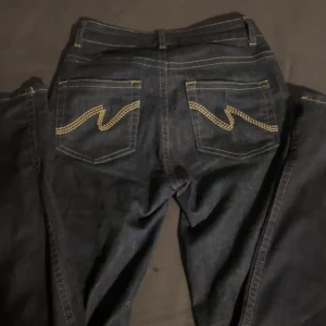 Replay mörkblå jeans med kontrastsöm - Snygga mörkblå jeans från Nelly med klassisk femficksdesign och coola kontrastsömmar på bakfickorna. Jeansen har guldfärgade detaljer och raka ben, samt tydliga stickningar längs kanterna. Perfekt för dig som gillar stilrena och tidlösa jeans.