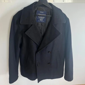 Svart skepparkavaj från American Eagle - Klassisk svart skepparkavaj från American Eagle med bred krage och dubbelknäppning. Jackan har två snedställda fickor framtill och är fodrad med quiltat innerfoder. Perfekt för kyliga dagar och ger en stilren look. Vid frågor och funderingar är det bara att skicka ett meddelande! Pris går att diskuteras!!