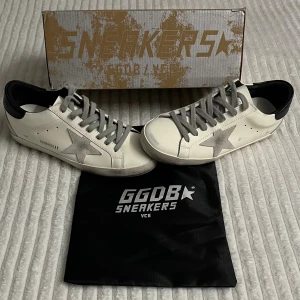 Golden Goose  - Säljer ett par vita Golden Goose med en fin grå stjärna på sidan, svarta detaljer vid hälen och härliga gåta snören. Skorna har en klassisk låg sneakersmodell och är tillverkade av skinn med slitna detaljer för et mer avslappnat utseende. Perfekt för nuvarande vinter men även kommande vår och sommar. Ett till ett .Skorna är helt nya och säljs på grund av fel storlek. Nypris ligger på ca 5500kr. Vid några frågor är det bara att skriva