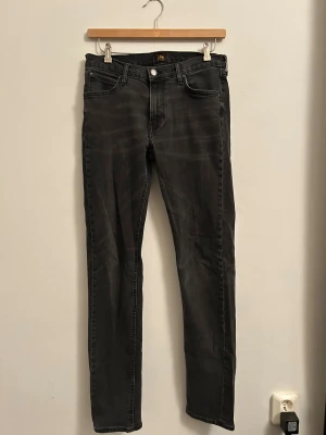 Svarta skinny jeans från Lee - Säljer ett par svarta skinny jeans från Lee med klassisk femficksdesign och Lee-logga på knapp och bakficka. Jeansen har smal passform och är tillverkade i stretchig denim för en bekväm känsla. Perfekta för dig som gillar en stilren look.