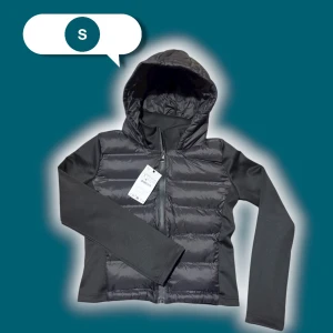 Svart pufferjacka med huva, stl S - Svart pufferjacka i storlek S med huva och dragkedja framtill. Jackan har quiltade partier på framsidan och släta ärmar i syntetmaterial. Perfekt för kyliga dagar och enkel att matcha med det mesta.