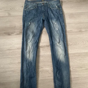 Blå jeans från Lee med slitningar - Säljer ett par blå jeans från Lee med coola slitningar och tvättade detaljer på både fram- och baksida. Klassisk femficksmodell med kontrastsömmar och läderpatch bak. Jeansen har rak passform och normal midja, tillverkade i robust denim. Skriv för mer bilder med mera 