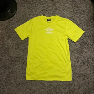 Gul fotbollströja från Umbro S - Snygg gul fotbollströja från Umbro i storlek S. Tröjan är tillverkad i 100% polyester och har en klassisk passform med korta ärmar och rund hals. Umbro-loggan är tryckt på bröstet och nacken. Perfekt för träning eller match. Har några fläckar (se bild)