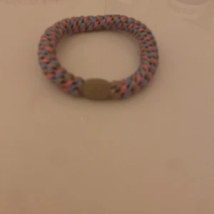 Färgglatt flätat armband från Kreafunk - Säljer ett snyggt armband från Kreafunk med flätad design i beige, blått och rosa. Armbandet har en rund form och ett diskret spänne med märkets logga. Perfekt accessoar för dig som gillar färg och en sportig stil.