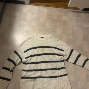 Vit stickad randig tröja från 157 - Säljer en vit stickad tröja från 157 i storlek L. Tröjan har svarta horisontella ränder och en ribbad hög hals. Den är långärmad och har en loose passform, perfekt för att chilla eller hänga med kompisar. Klassisk och enkel design som funkar till många stilar. Mindre i storleken 