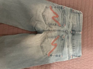 Ljusblå jeans från Nelly med rosa detalj - Snygga ljusblå jeans från Nelly, bootcut har används 1-2 gånger,  rosa detalj på fickor och gylf med två knappar!! pris går att ändra.                      ( utan hål)