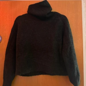 Svart polotröja i stickad ull - Mysig svart polotröja med hög krage och långärmad modell. Stickad i mjuk ull som håller dig varm under kyliga dagar. Perfekt för dig som gillar en enkel och stilren look med lite oversized känsla.