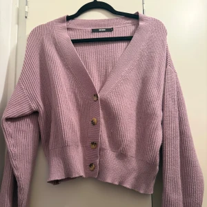 Ljuslila ribbad kofta från Bik Bok - Superfin ljuslila kofta från Bik Bok i ribbstickad kvalitet. Croppad modell med v-ringning och fyra snygga knappar framtill. Perfekt att slänga över en topp för en chill look. Långärmad och mjuk, passar dig som gillar pastellfärger.