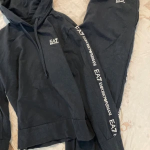 Svarta mjukisbyxor EA7 Emporio Armani- NYA - Svarta mjukisbyxor från EA7 Emporio Armani med vit logga längs benet. Byxorna har en avslappnad passform och är gjorda i mjukt bomullsmaterial. Snyggt sportigt snitt och elastisk midja för extra komfort. Perfekta för chill eller träning. L/XL