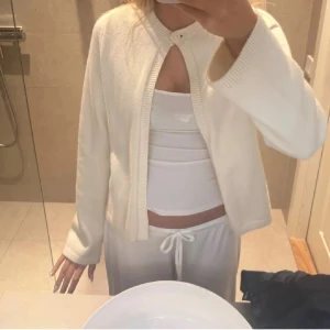 Vit kofta med knapp i halsen - Säljer en stilren vit kofta med rund halsringning och en enkel knapp högst upp. Koftan har långa ärmar och ribbade kanter, perfekt att slänga över ett linne eller topp. Enkel och clean look som passar till mycket.💞💞