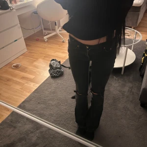Svarta bootcut jeans med slitna knän - Säljer ett par svarta jeans med bootcut och egen gjorde hål, mid waist går att sy ner hemma om man vill💖
