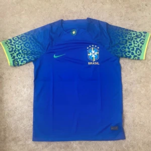 Blå Brasilien fotbollströja Nike - Säljer en blå Brasilien fotbollströja från Nike med korta ärmar och leopardmönster i grönt och blått på ärmarna. Tröjan har Brasil-logga och Nike swoosh på bröstet. Materialet är lätt och andas, perfekt för match eller träning.