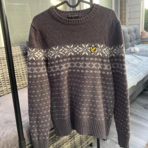 Grå stickad tröja Lyle & Scott S - Mysig grå stickad tröja från Lyle & Scott i storlek S. Tröjan har ett snyggt vitt vintermönster över bröstet och armarna samt den klassiska gula fågel-loggan på vänster sida. Rund hals och ribbade muddar för extra komfort.