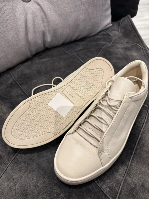 Vita sneakers från Vagabond - Säljer ett par stilrena vita sneakers från Vagabond med rund tå och platt sula. Skorna har snörning och är tillverkade i mjukt skinn med diskreta sömmar och minimalistisk design. Perfekta för dig som gillar cleana och klassiska sneakers.
