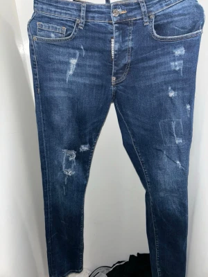 Blå distressed jeans från Dsquared2 - Snygga blå jeans från Dsquared2 med slitna detaljer och klassisk femficksdesign. Jeansen har normal passform, raka ben och är tillverkade i jeansmaterial. Perfekta för dig som gillar en cool och avslappnad stil.